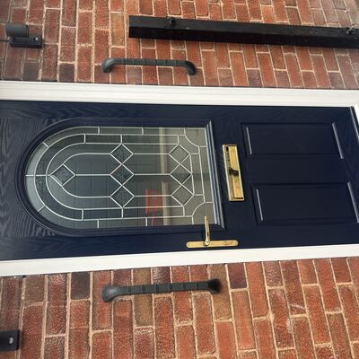 Newly fitted navy composite front door with decorative glass panel and gold handle.