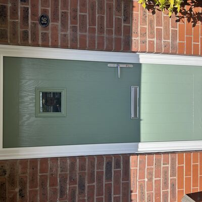 Newly fitted sage green composite front door with small square glass panel and silver handle.