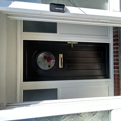 Newly fitted black composite front door with decorative circular glass, gold handle and white side panels.