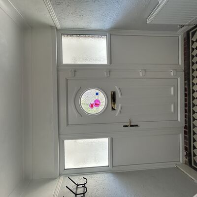 Newly fitted white uPVC front door with decorative circular glass, gold handle and white side panels.